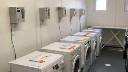 Waschküche mit fünf Waschmaschinen, grauem Noppenboden, weißen Wänden, zwei Sanitärfenstern in einem Containerbüro-Modulbau