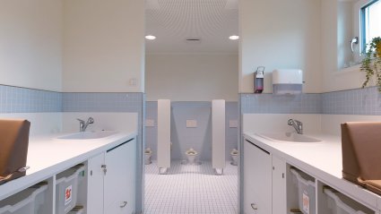 Großzügiger Sanitärbereich in einem Kindergarten-Modulbau mit kindgerechten Toiletten, zwei Wickeltischzeilen mit integrierten Waschbecken und hellblauen Wand- und Bodenfliesen