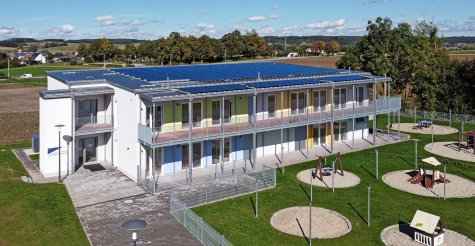 Drohnenaufnahme eines zweigeschossigen Kindergarten-Modulbaus mit überdachter Balkonanlage, Flachdach und PV-Analage