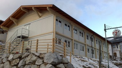 Zweigeschoßige Wohncontainer-Anlage aus weißen Modulen mit Geschoß- und Etagenverkleidung aus Holz, Fluchttreppe und Satteldach