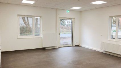 Gruppenraum in einem Kindergarten-Container mit braunem Vinylboden, wei&szlig;en W&auml;nden, Terrassent&uuml;r, Fenstern und Akustikdecke