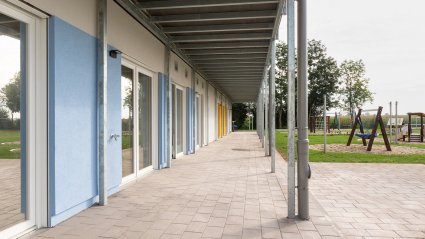 Überdachter und gepflasterter Terrassenbereich eines zweistöckigen Kindergarten-Modulbaus mit Spielplatz