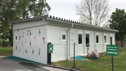 Außenansicht einer Kindergarten-Containeranlage bestehend aus sechs weißen 20-Fuß-Modulen, mit Pultdach Attika und Wellblecheindeckung
