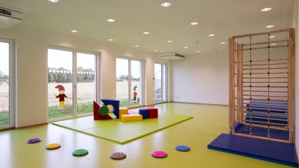Bewegungsraum in einem Kindergarten-Modulbau mit gr&uuml;nem Boden, wei&szlig;en W&auml;nden, Akustikdecke, vier Terrassent&uuml;ren und kindgerechten Turnm&ouml;bel