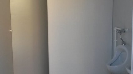 Innenansicht des Herren-WC in einem Sanit&auml;rcontainer mit Urinal, wei&szlig;er WC-Wand und dunkelgrauem Vinylboden