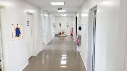 Flurbereich in einem Kindergarten-Modulbau mit hellbraunem Boden, weißen Wänden, weißen Türen und Akustikdecke