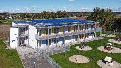 Drohnenaufnahme eines zweigeschossigen Kindergarten-Modulbaus mit überdachter Balkonanlage, Flachdach und PV-Analage