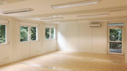 Innenaufnahme eines leeren Gruppenraumes in einer Schulcontainer-Anlage mit hellbraunem Vinylboden und wei&szlig;en W&auml;nden