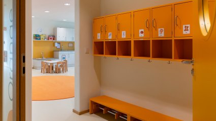 Garderobenbereich in einem Kindergarten-Modulbau mit kindgerechter Möblierung, orange Sitzbank und orange Wandregale mit Garderobenhaken