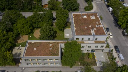 Drohnenaufnahme eines dreigeschossigen Schulcontainer-Modulbaus mit Holzfassade, Gründach, Spiel- und Grünflächen