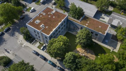 Drohnenaufnahme eines dreigeschossigen Schulcontainer-Modulbaus mit Holzfassade, Gründach, Spiel- und Grünflächen