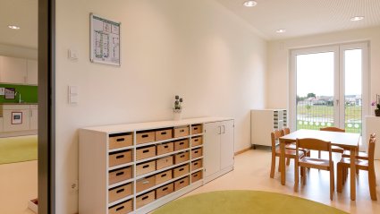 Werkraum in einem Kindergarten Modulbau mit kindgerechter Möblierung, grünem Teppich und Balkontür