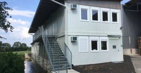 Zweistöckige Bürocontaineranlage aus weißen Modulen mit Außentreppe, Zugangspodest und Pultdach