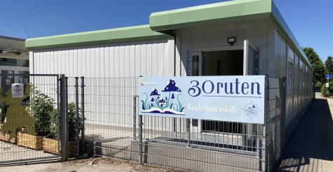 Überdachter Eingangsbereich eines eingeschoßigen Kindergarten-Modulbaus bestehend aus weißen Raummodulen mit grüner Attika