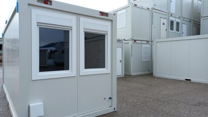 Wei&szlig;er 20-Fu&szlig; K&uuml;chencontainer mit zwei Rollladenfenstern sowie Strom- und Wasseranschluss an der Stirnseite
