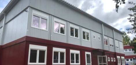 Zweigeschoßige Schulcontainer-Anlage in Modulbauweise mit roten Schulcontainern im Erdgeschoß und grauen Schulcontainern im Obergeschoß, Eingangsbereich, Pultdach