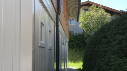 Seitenansicht eines zweistöckigen Wohncontainer-Modulbaus mit weißen Modulen im Erdgeschoß und Holzfassade im Obergeschoß