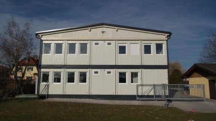 Au&szlig;enaufnahme der R&uuml;ckseite eines zweigeschossigen Schulcontainer-Modulbaus aus wei&szlig;en Raumelementen, mit Satteldach und Attika