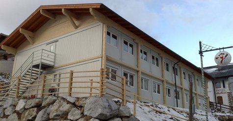 Zweigeschoßige Wohncontainer-Anlage aus weißen Modulen mit Geschoß- und Etagenverkleidung aus Holz, Fluchttreppe und Satteldach