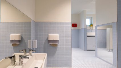 Großzügige Sanitäranlage in einem Kindergarten-Modulbau mit kindgerechter Ausstattung, Doppelwaschbecken, Wickeltisch, Wandspiegel und hellblaue Boden- und Wandfliesen