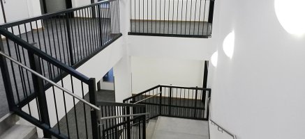 Betontreppe mit schwarzem Stahlgeländer und Edelstahlhandlauf in mehrstöckigem Modulgebäude