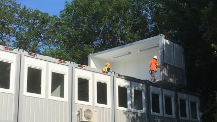 Zwei Arbeiter mit Helm und Schutzausrüstung die einen Container vom Kran zur Montage im dritten Geschoß übernehmen