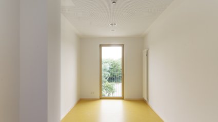 Innenaufnahme eines Garderobenraumes in einem Schulcontainer-Modulgebäude mit gelbem Vinylboden, weißen Wänden und Balkontür