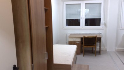 Innenaufnahme einer Personalunterkunft in einer Wohncontainer-Anlage, ausgestattet mit einem Bett, Kasten, Schreibtisch und einem Doppelfenster
