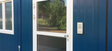 Modulbau aus blau lackierten Containern mit weißer Nebeneingangstür, Licht, Bewegungsmelder und Fenstern