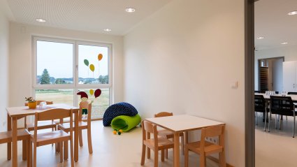 Nebenraum in einem Kindergarten-Modulbau mit bodenebenem Doppelfenster, zwei Tischen und Stühlen zum Teil in kindgerechter Ausführung