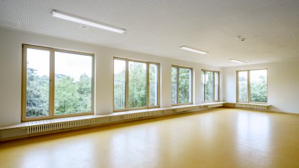 Großzügiger Gruppenraum in einer Schulcontainer-Anlage mit Fensterzeile und Sitzgelegenheit, gelbem Vinylboden, weißen Wänden und Akustikdecke mit LED-Leuchten