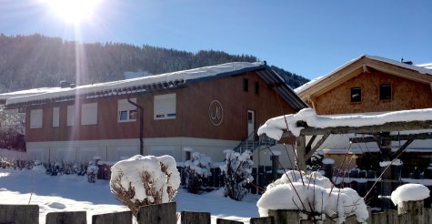 Zweigeschoßiger Wohncontainer-Modulbau mit weißen Modulen im Erdgeschoß, Holzfassade im Obergeschoß, Außentreppe und Satteldach