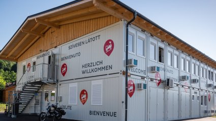 R&uuml;ckansicht eines zweist&ouml;ckigen Containerb&uuml;ros aus wei&szlig;en Containern mit Beklebung, Au&szlig;entreppe mit Zugangspodest und Satteldach mit Holzverkleidung