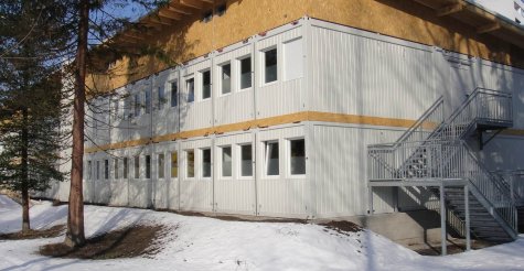 Au&szlig;enaufnahme eines Krankenhaus-Modulbaus aus wei&szlig;en Modulen, mit Fluchttreppe, Pultdach und Attika mit Holzverkleidung